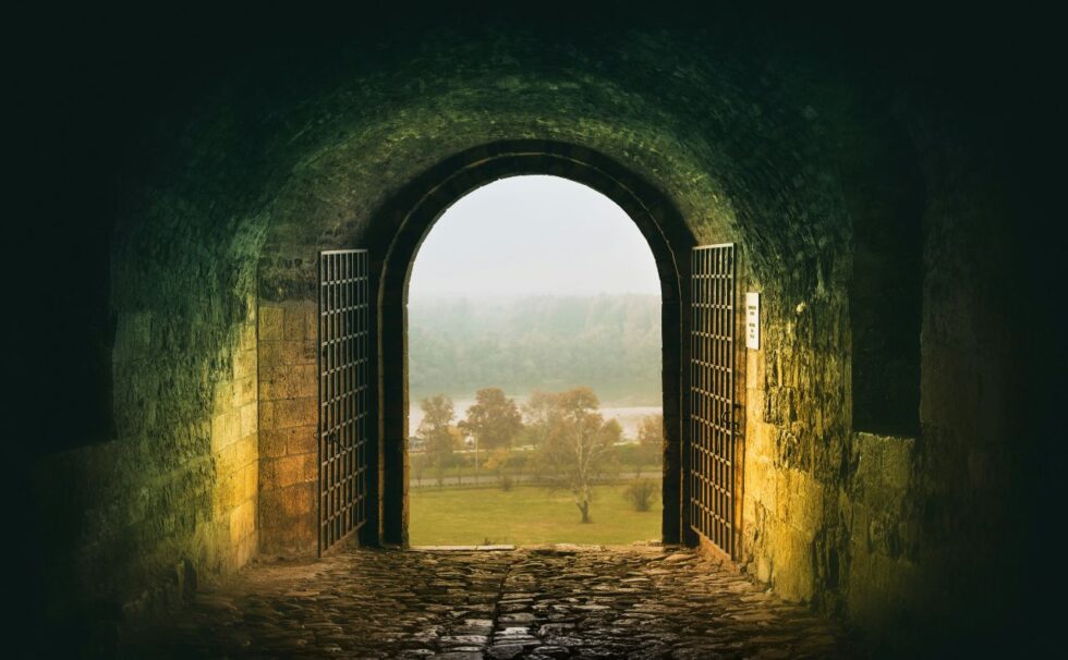 Zdjęcie przedstawia kamienną bramę wychodzącą na krajobraz z drzewami i rzeką lub jeziorem.