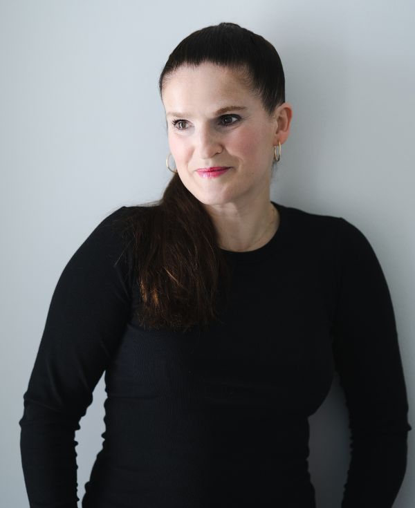 Kobieta o czarnych włosach, pomalowanych na czerwono ustach, w czarnej bluzce.