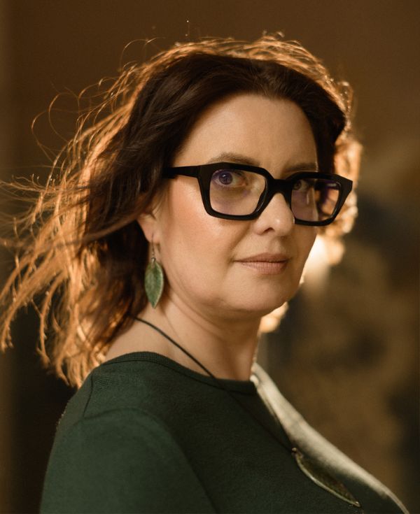 Kobieta w okularach, w zielonej bluzce i w kolczykach.