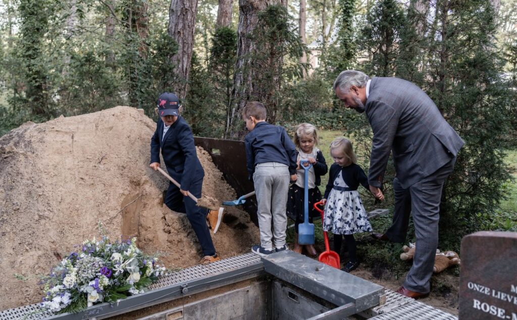 Dzieci i jeden dorosły nad grobem z łopatami w dłoniach przy górce z piasku